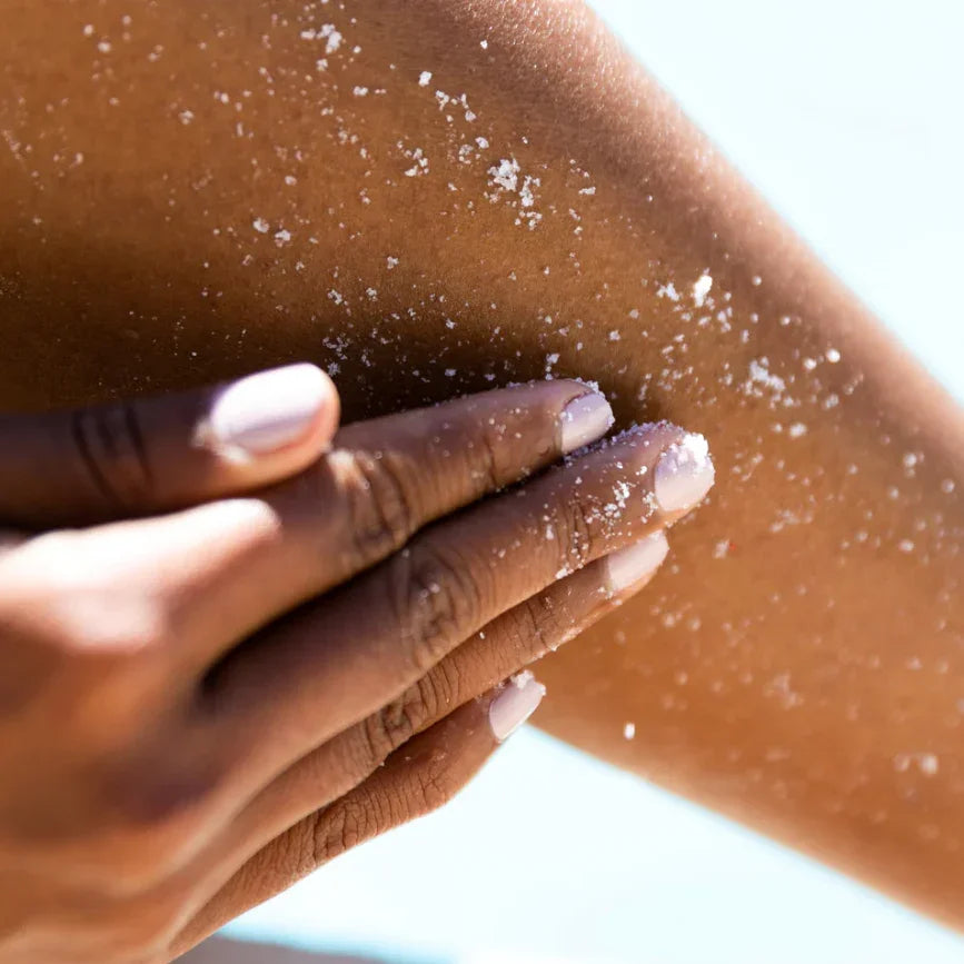 Hand applying salt scrub to sun-kissed skin for gentle exfoliation and relaxation