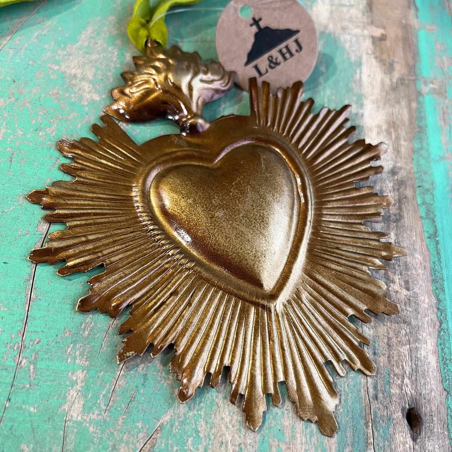 Golden sacred heart ornament with radiant rays on a green velvet ribbon.