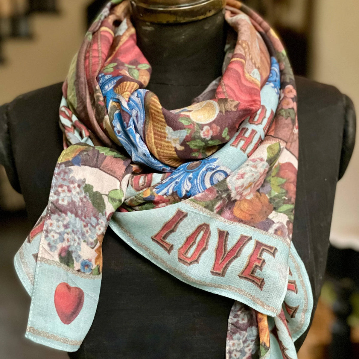 Colorful heart-themed scarf with 'LOVE' print, floral patterns, and vintage design, styled on mannequin for romantic gift ideas.