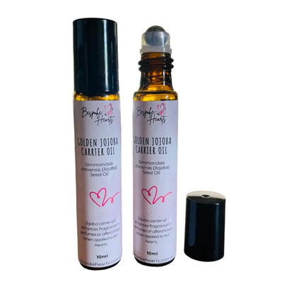 Two bottles of Golden Jojoba Carrier Oil on a wooden surface with a blurred indoor background.