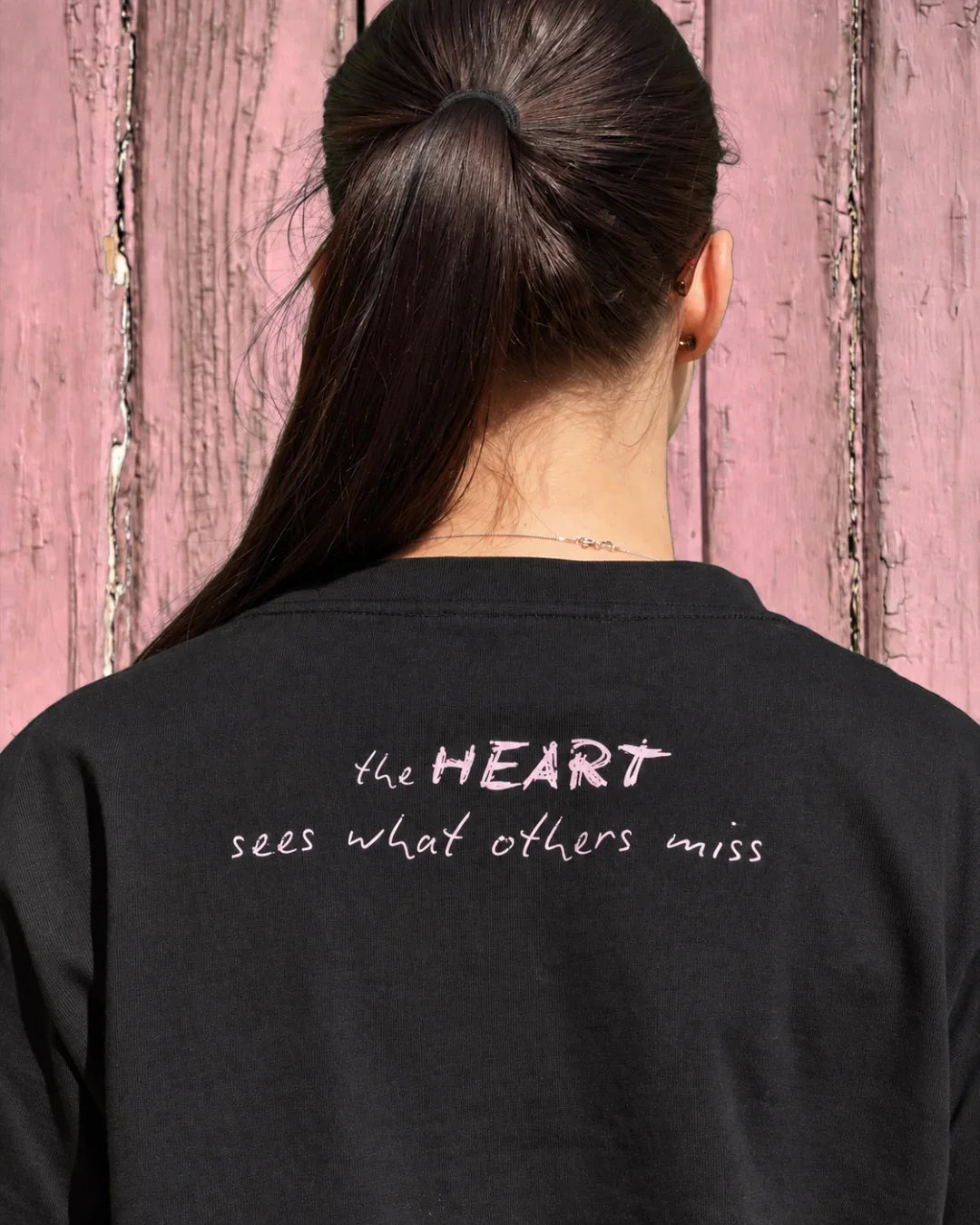 Back view of a person wearing a Bespoke Hearts black tee with 'the HEART sees what others miss' text.