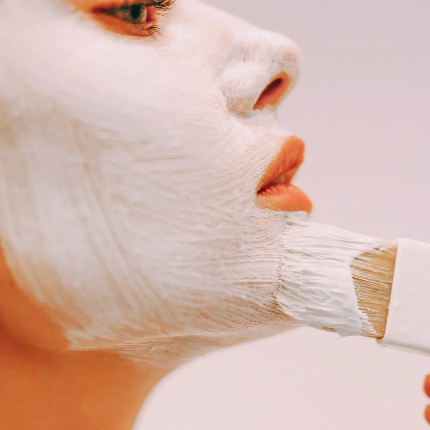 Woman applying white face mask with brush for skincare routine