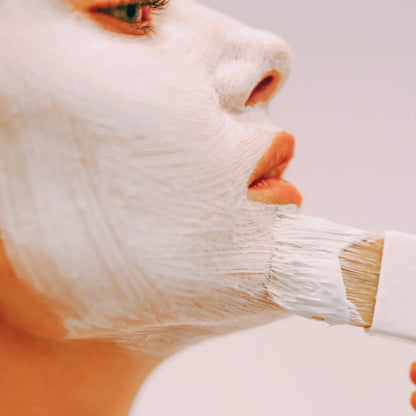 Woman applying white face mask with brush for skincare routine